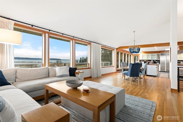 living room featuring a water view, an inviting chandelier, light wood-type flooring, and vaulted ceiling