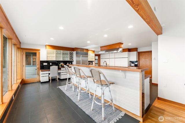 kitchen featuring a sink, a peninsula, built in fridge, and a kitchen breakfast bar