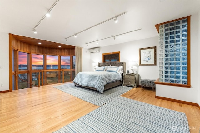 bedroom featuring rail lighting, baseboards, wood finished floors, and a wall mounted air conditioner