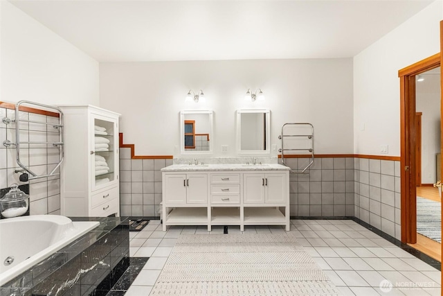 bathroom featuring tile patterned flooring, a wainscoted wall, a sink, tile walls, and double vanity