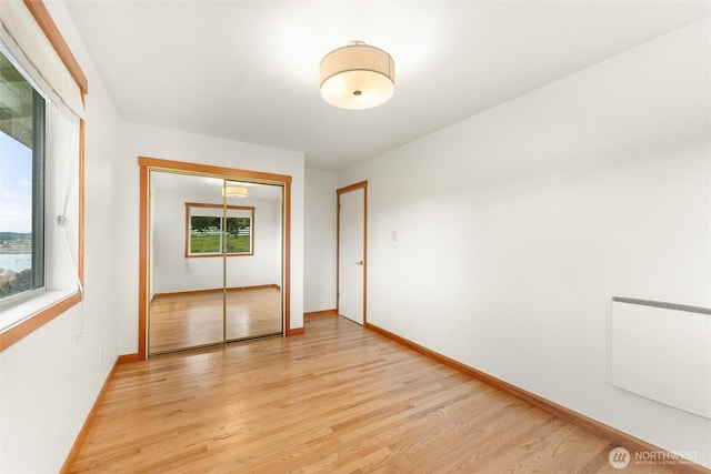 unfurnished bedroom with a closet, multiple windows, baseboards, and light wood finished floors