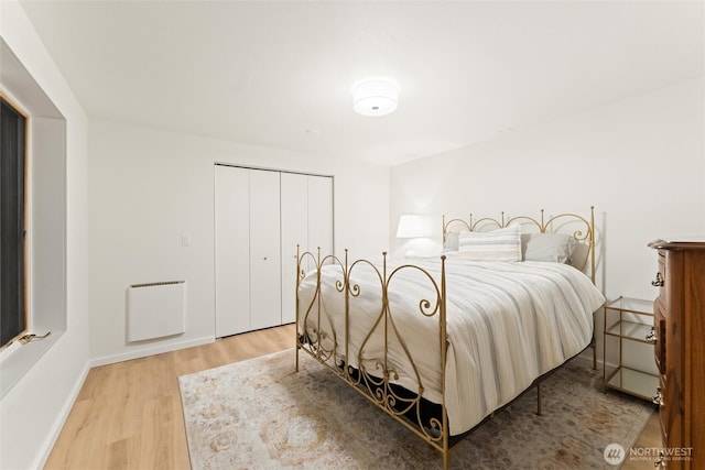 bedroom with light wood-style floors, a closet, baseboards, and heating unit