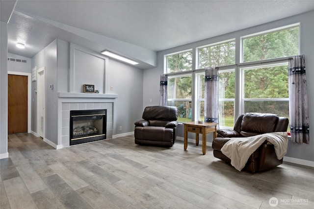 living area featuring a textured ceiling, a fireplace, wood finished floors, visible vents, and baseboards