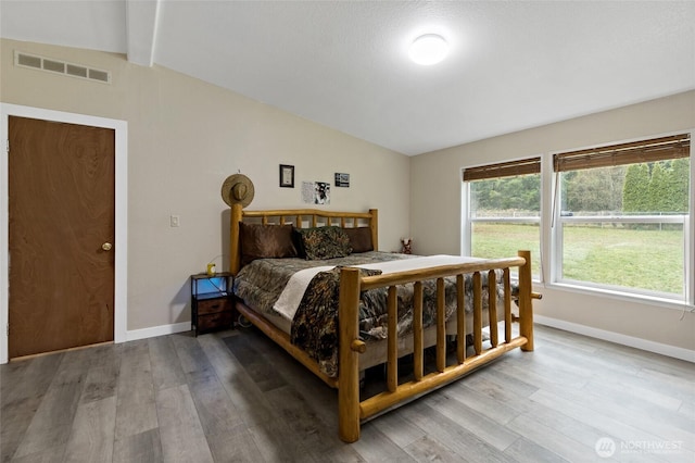 bedroom with visible vents, lofted ceiling with beams, baseboards, and wood finished floors