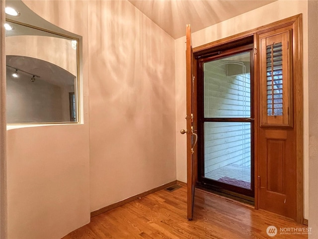 entrance foyer with arched walkways, visible vents, baseboards, and wood finished floors