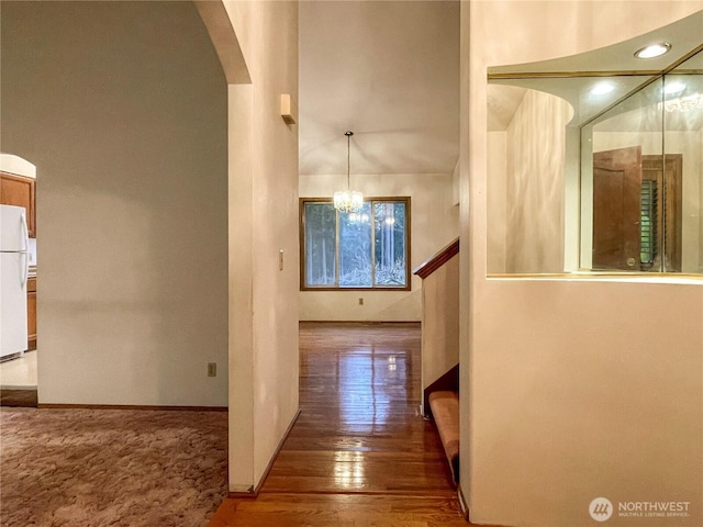 hall with baseboards, a notable chandelier, arched walkways, and wood finished floors