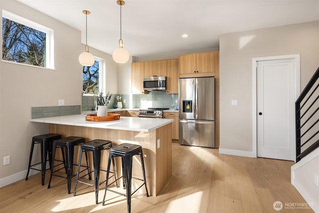 kitchen featuring light wood finished floors, decorative backsplash, a breakfast bar, a peninsula, and stainless steel appliances