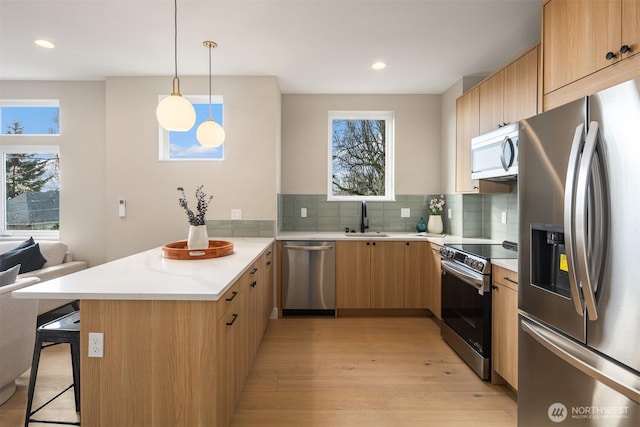 kitchen with a breakfast bar, light countertops, appliances with stainless steel finishes, a sink, and a peninsula