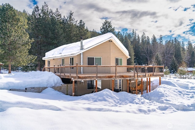 snow covered rear of property featuring a wooded view and a wooden deck