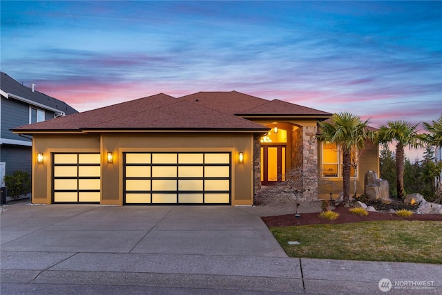 prairie-style house featuring a garage, a shingled roof, driveway, and stucco siding