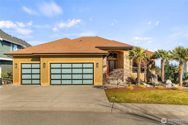 view of front facade featuring roof with shingles, a garage, driveway, and stucco siding