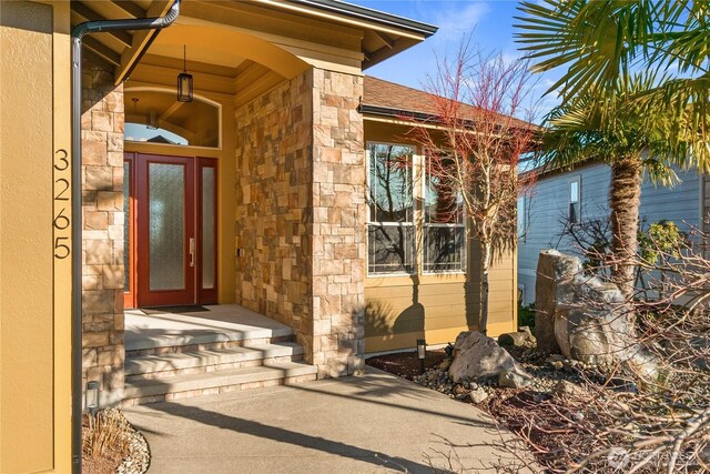 view of exterior entry with stone siding and roof with shingles