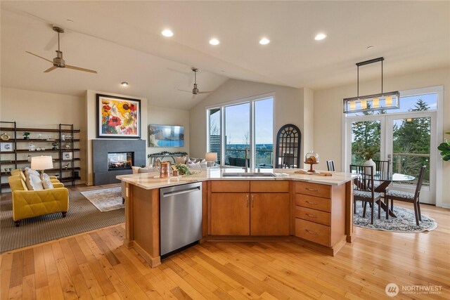 kitchen with open floor plan, dishwasher, a tile fireplace, light wood-style floors, and a sink