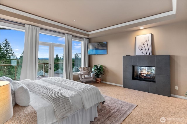 carpeted bedroom with a tray ceiling, baseboards, ornamental molding, and a tiled fireplace