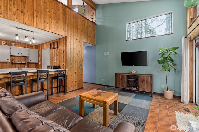 living room with tile patterned flooring, visible vents, wood walls, and a high ceiling