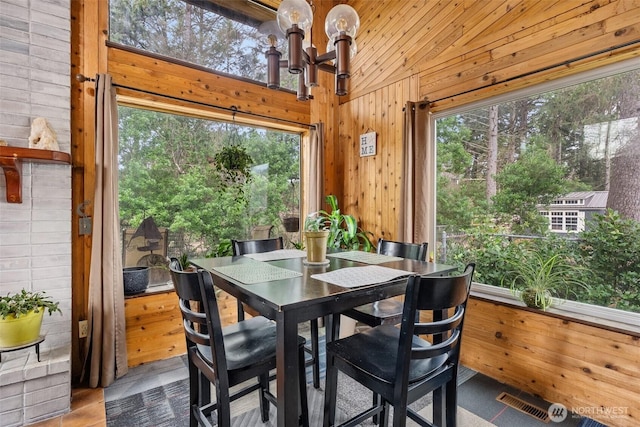 dining area featuring a chandelier, vaulted ceiling, visible vents, and wood walls