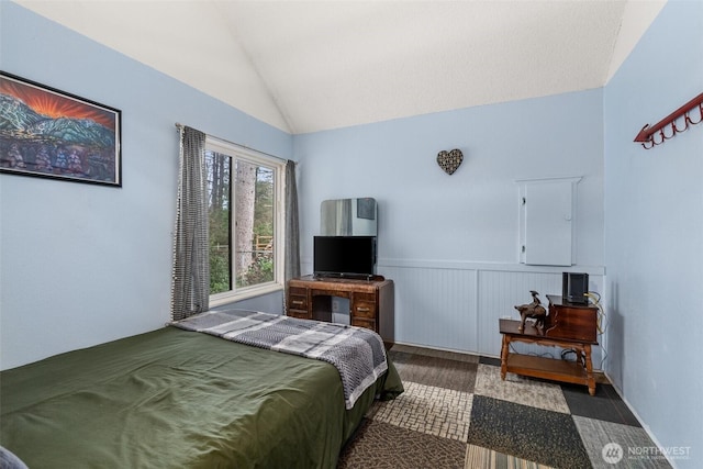 bedroom featuring lofted ceiling and a wainscoted wall