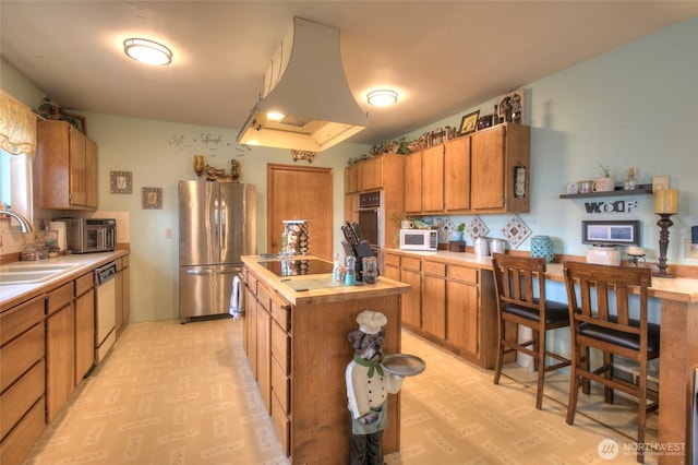 kitchen featuring a center island, island exhaust hood, stainless steel appliances, brown cabinetry, and a sink