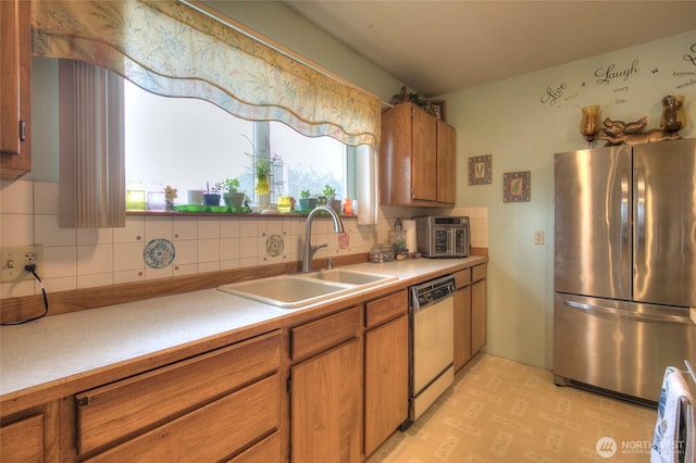 kitchen with dishwasher, brown cabinets, a sink, and freestanding refrigerator