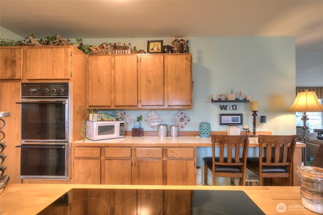 kitchen featuring brown cabinets, light countertops, dobule oven black, and white microwave