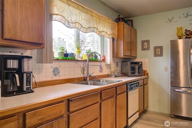 kitchen featuring light countertops, a sink, freestanding refrigerator, backsplash, and dishwasher