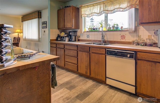 kitchen with white dishwasher, a healthy amount of sunlight, light wood-type flooring, and a sink