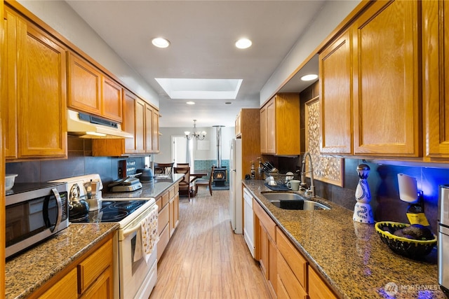 kitchen with a skylight, brown cabinetry, a sink, white appliances, and under cabinet range hood