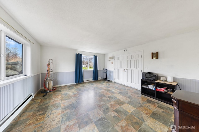 interior space featuring a baseboard radiator, stone finish floor, and wainscoting