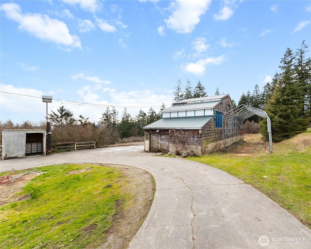 view of front of property featuring an outbuilding, metal roof, driveway, and fence