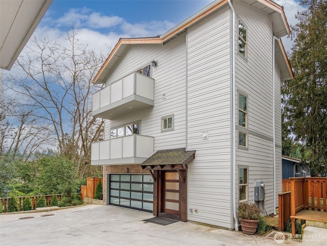 view of property exterior with a balcony, an attached garage, and concrete driveway