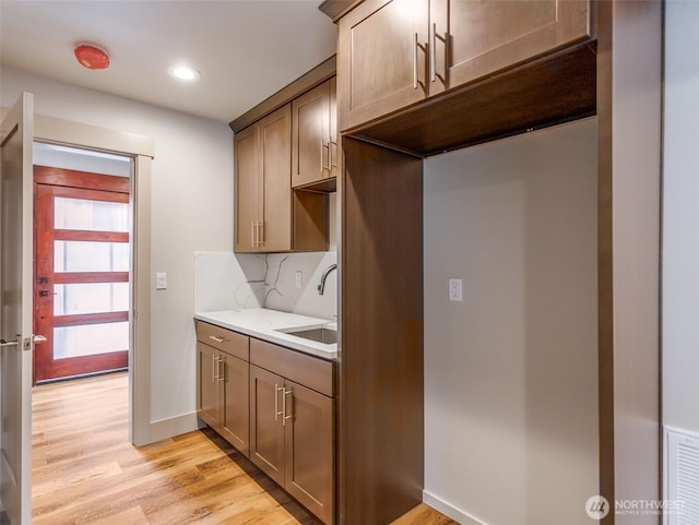 kitchen featuring light wood-style flooring, a sink, light countertops, backsplash, and recessed lighting