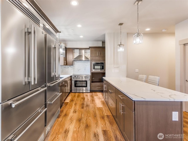 kitchen with a center island, high end appliances, backsplash, wall chimney range hood, and light wood-type flooring