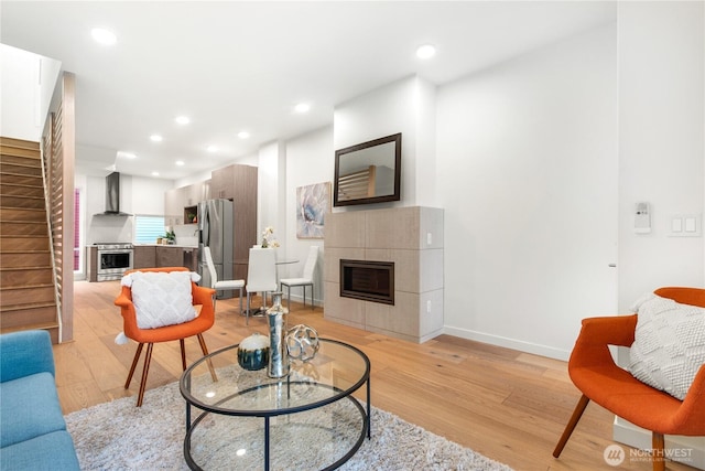 living room featuring recessed lighting, baseboards, stairs, light wood-type flooring, and a tiled fireplace