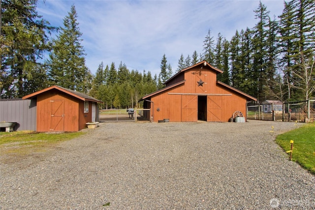 view of barn with a gate, fence, and gravel driveway