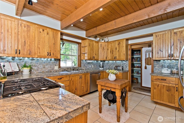 kitchen with light tile patterned floors, a sink, stainless steel dishwasher, backsplash, and beamed ceiling