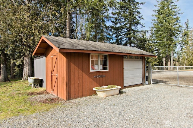 view of outbuilding with a garage, an outdoor structure, and fence