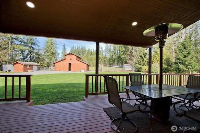 deck featuring a barn, a lawn, fence, outdoor dining area, and an outdoor structure