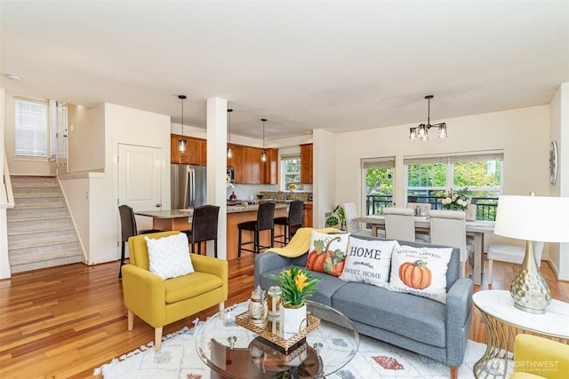 living room with stairway, light wood finished floors, and an inviting chandelier