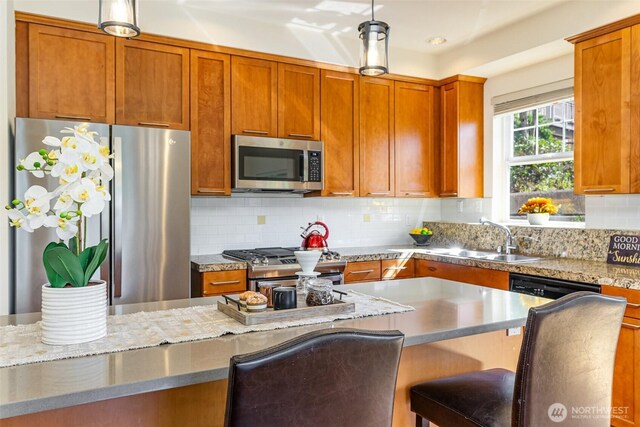 kitchen featuring stainless steel appliances, a sink, light stone countertops, tasteful backsplash, and decorative light fixtures