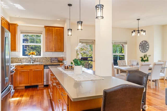 kitchen with wood finished floors, stainless steel appliances, a sink, and decorative light fixtures