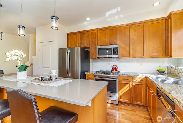 kitchen featuring stainless steel appliances, a breakfast bar, a sink, a center island, and decorative light fixtures