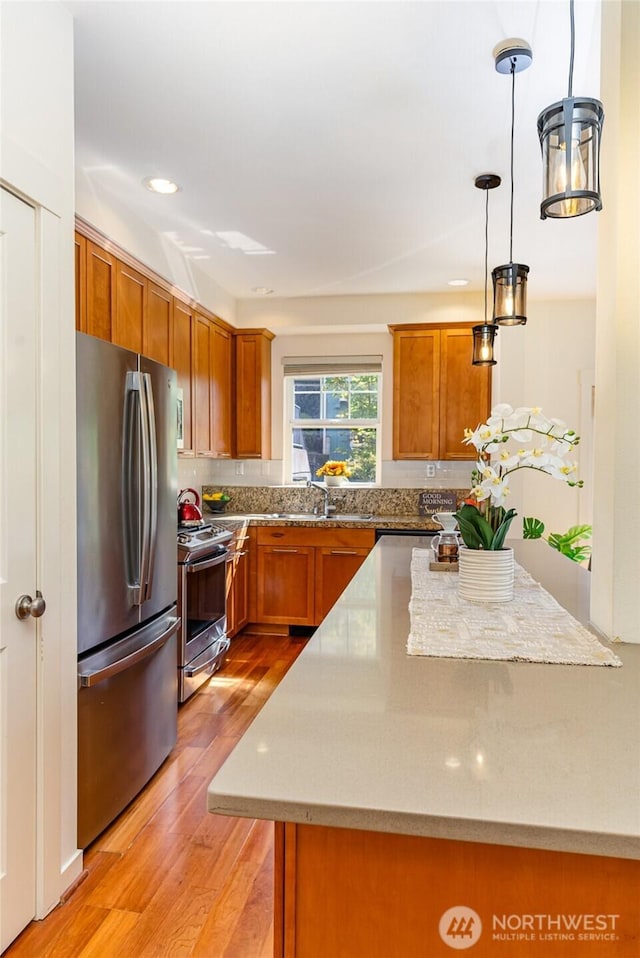 kitchen with appliances with stainless steel finishes, brown cabinets, a center island, light wood-type flooring, and pendant lighting