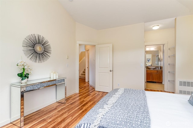 bedroom featuring baseboards, light wood-style flooring, radiator heating unit, and ensuite bathroom