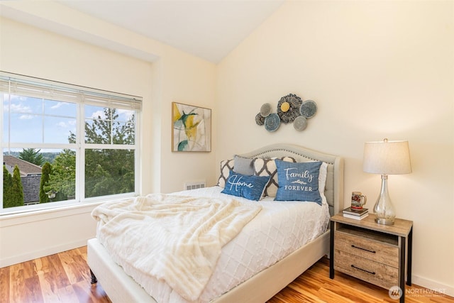 bedroom with light wood finished floors, baseboards, visible vents, and vaulted ceiling