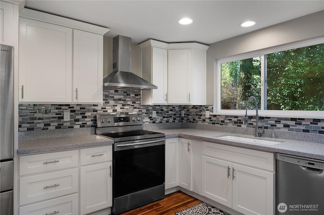 kitchen with a sink, white cabinetry, wall chimney range hood, appliances with stainless steel finishes, and tasteful backsplash