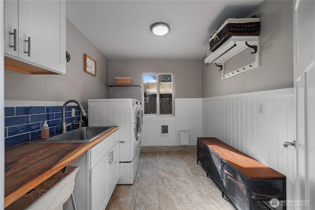 clothes washing area with independent washer and dryer, cabinet space, a sink, and a wainscoted wall