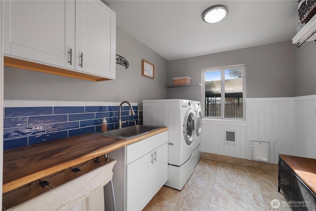 washroom featuring cabinet space, wainscoting, heating unit, washing machine and dryer, and a sink