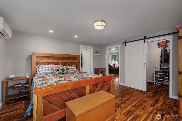 bedroom featuring a spacious closet, a barn door, wood finished floors, a wall mounted air conditioner, and baseboards