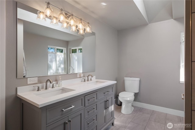 bathroom with toilet, double vanity, baseboards, and a sink