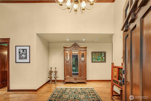 entryway featuring a towering ceiling, light wood-style floors, baseboards, and a chandelier